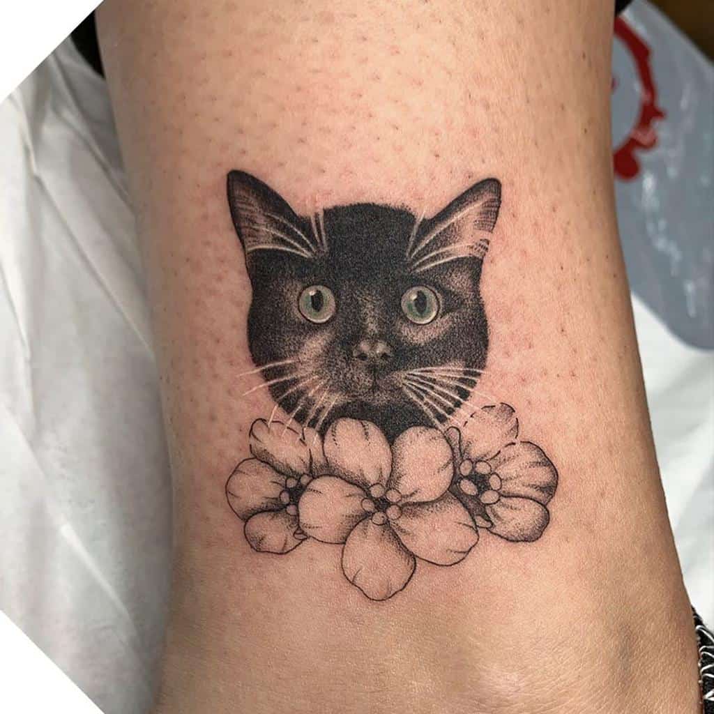 Tattoo of a cat's face with delicate flowers beneath it on a person's skin