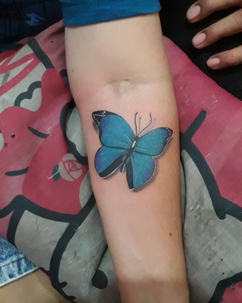 Forearm tattoo featuring a graceful blue butterfly, accentuated with black outlines and intricate details