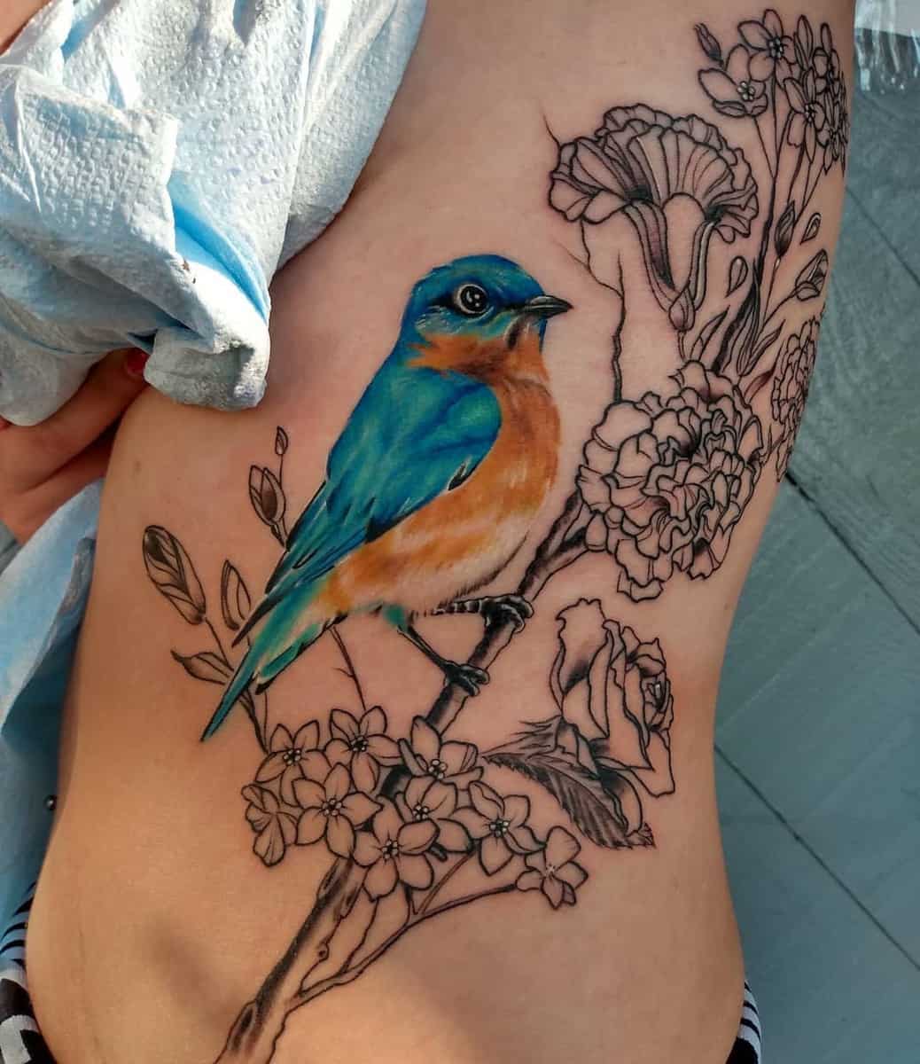 Colorful bird tattoo with flowers on a side featuring blue and orange feathers