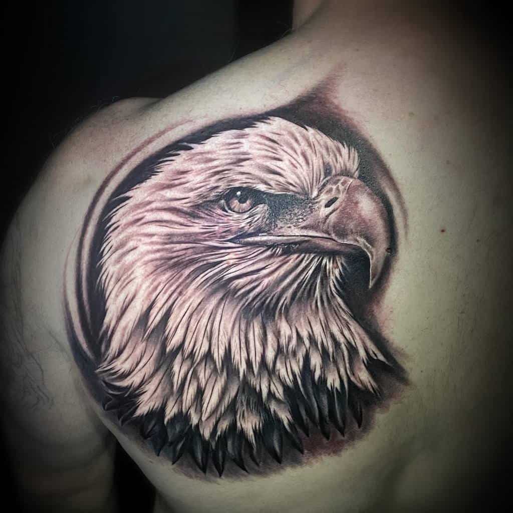 A detailed eagle head tattoo on an upper back and shoulder in grayscale shading