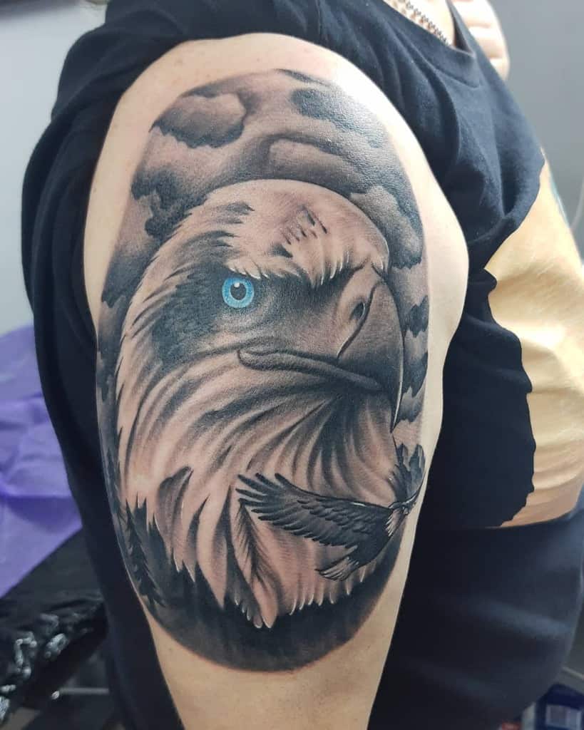 Tattoo of a realistic eagle with a blue eye and a smaller bird flying in front on an upper arm