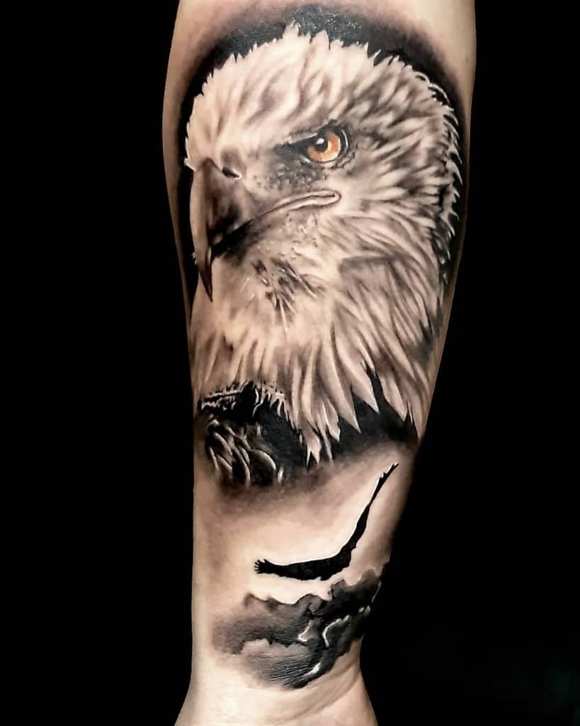 A detailed eagle tattoo, with a close-up of the eagle's head and a distant silhouette of a flying eagle below it