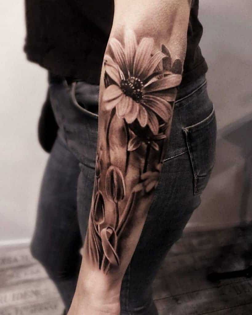 Forearm tattoo of a large daisy flower with buds and leaves in black and gray ink
