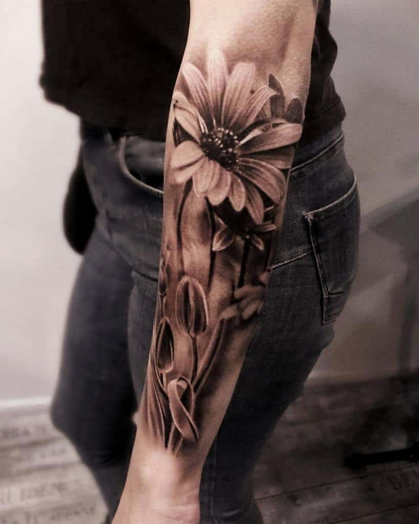 Realistic floral sleeve tattoo showcasing a detailed daisy with buds and stems, blending soft shading and intricate lines