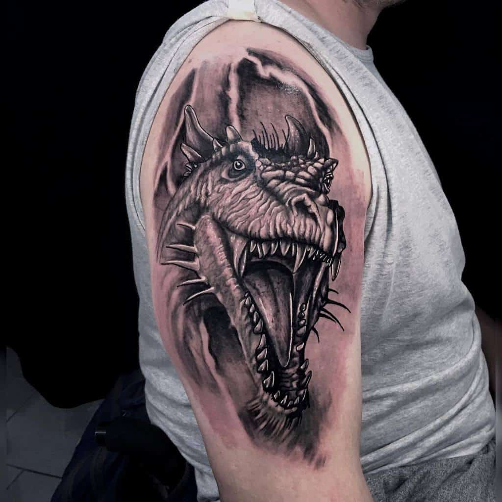Black and gray dragon tattoo on a person's upper arm, featuring an open-mouthed, roaring dragon