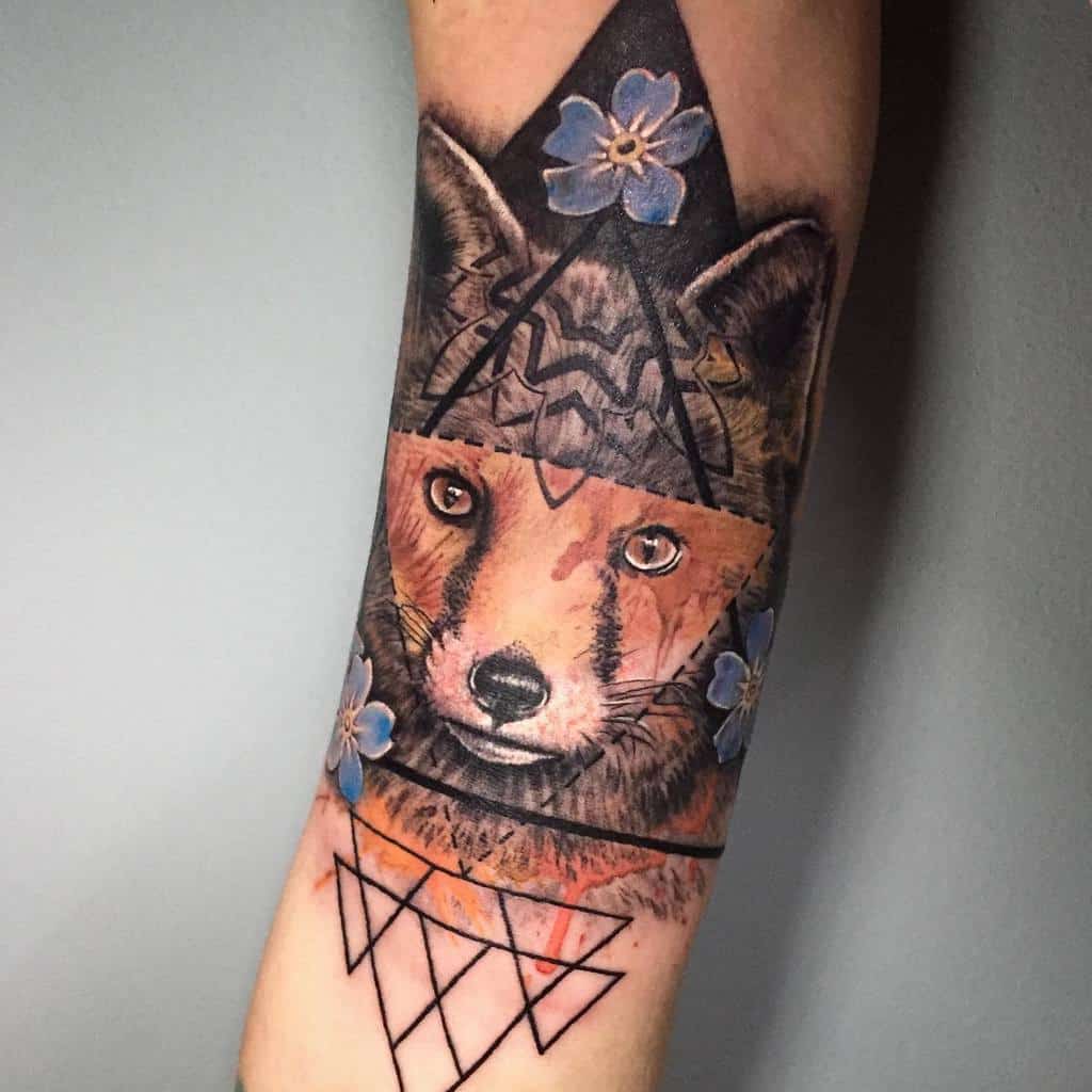 A vibrant fox tattoo featuring a realistic face, geometric patterns, and delicate blue flowers for contrast