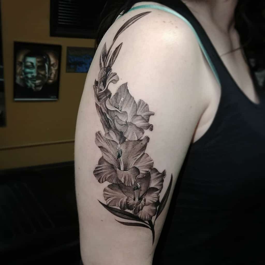 A woman's arm tattoo depicting detailed black and grey gladiolus flowers
