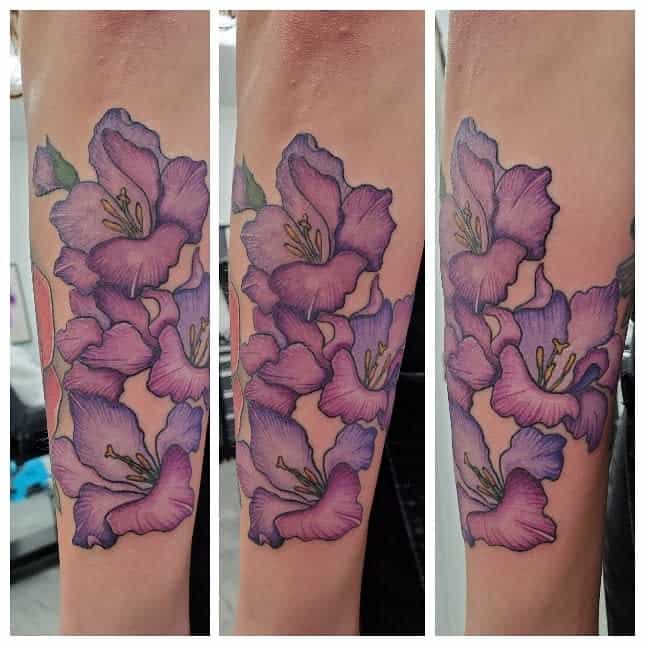Tattoo of purple gladiolus flowers on an arm, depicted in a triptych view showing different angles