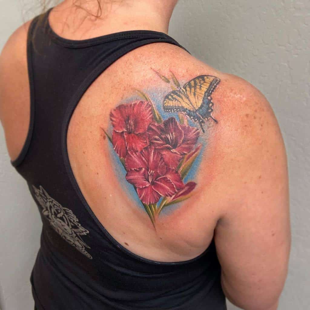 A person with a tattoo of red gladiolus flowers and a butterfly on their upper back