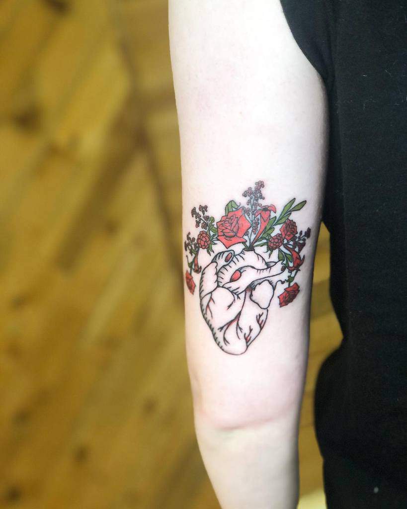 Tattoo of an anatomical heart with blooming flowers on the forearm