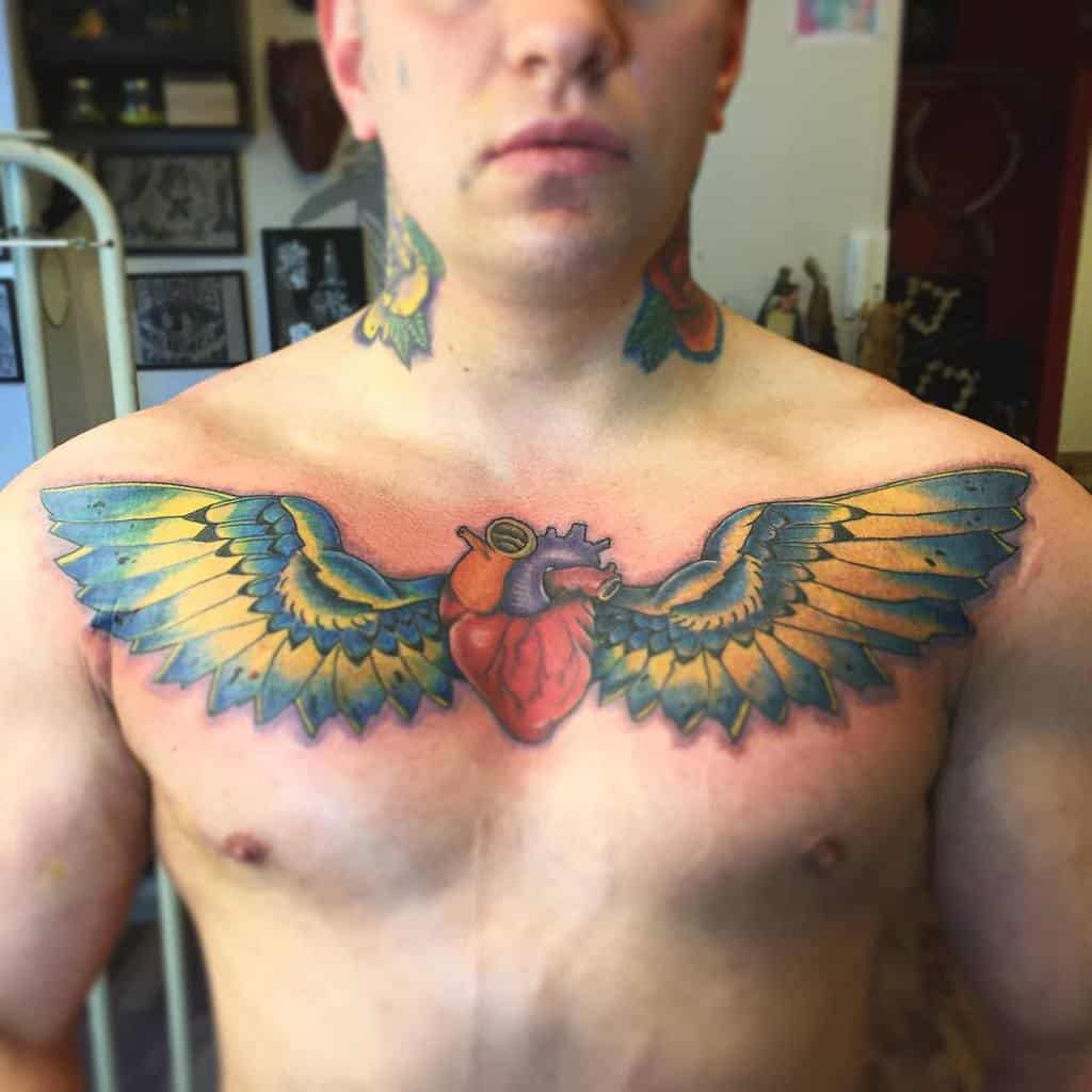 A person with a chest tattoo featuring a heart with wings spread outwards stands in the room, exuding an aura of quiet strength and individuality