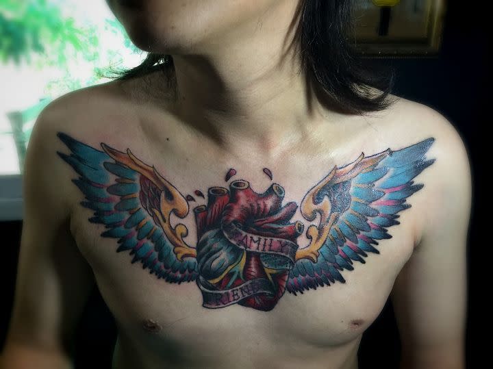 Tattoo of a heart with wings and a banner gracefully adorning the chest