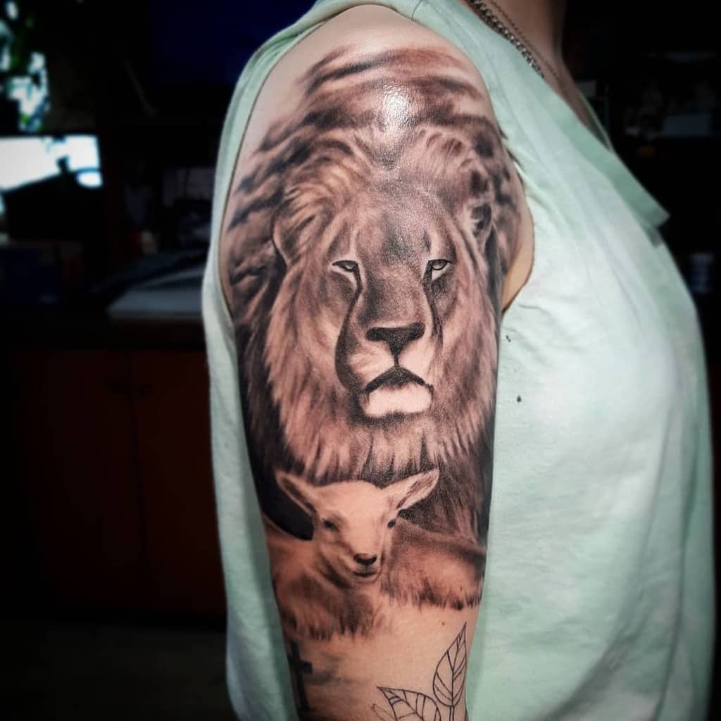 A person's upper arm tattoo featuring a majestic lion's head interwoven with the gentle image of a lamb