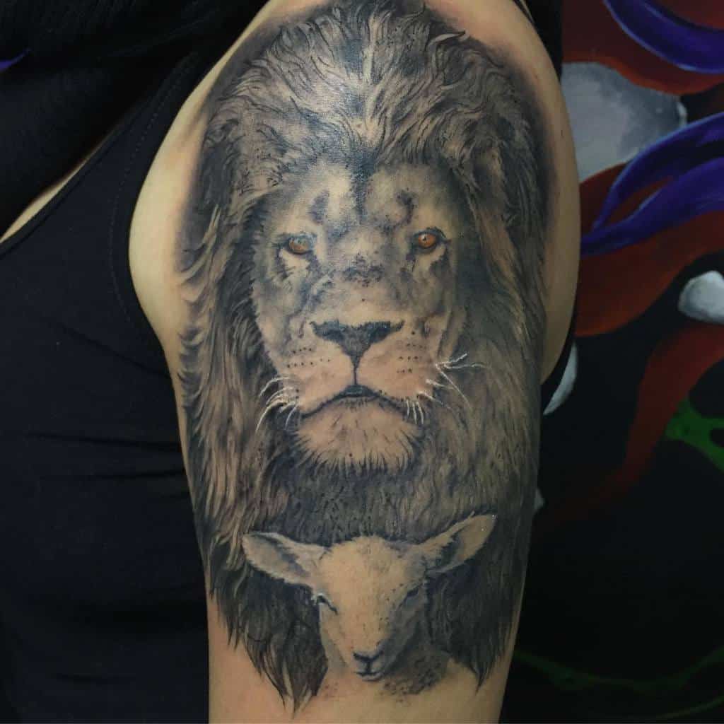 Tattoo of a lion’s face with a gentle lamb beneath it on a person’s upper arm