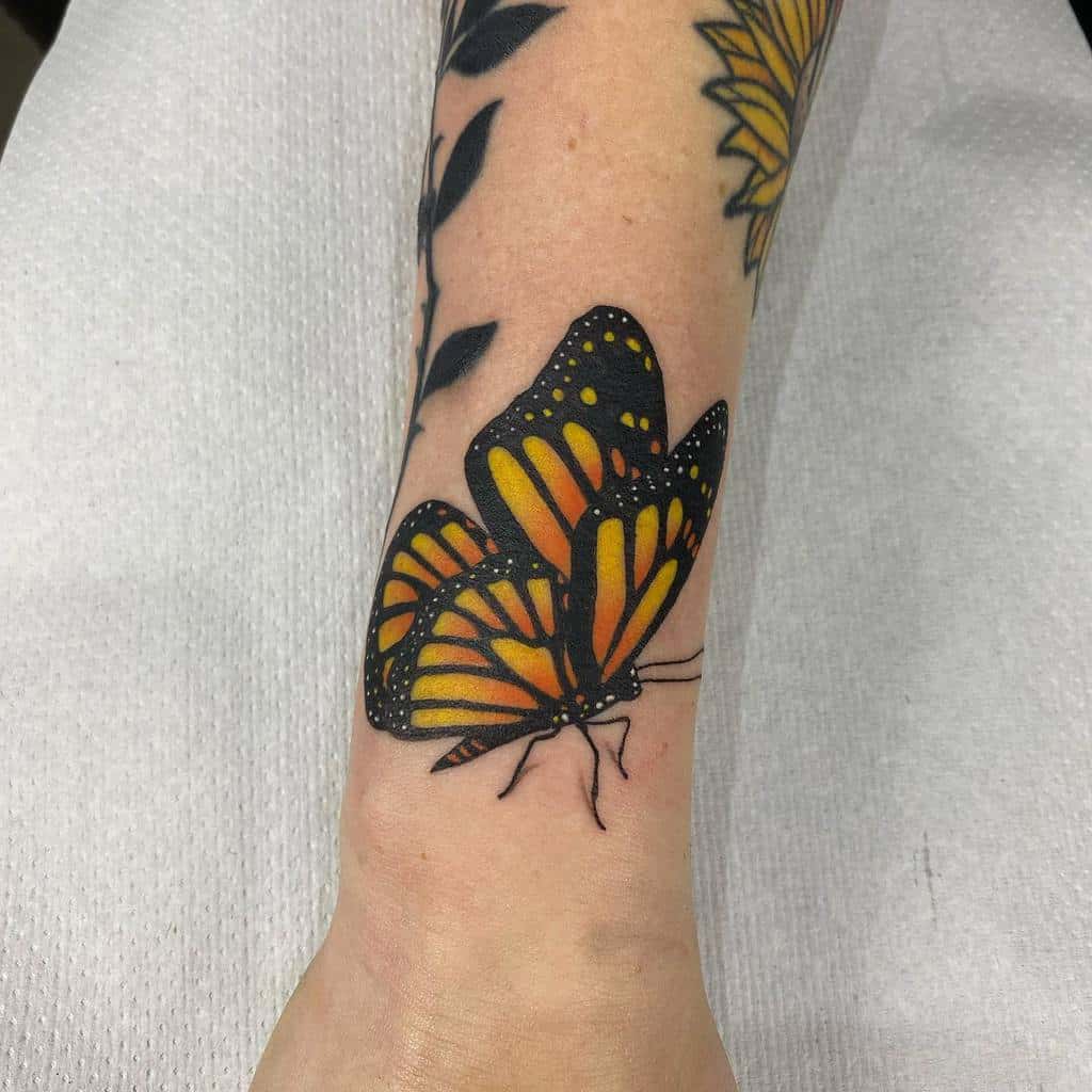 A vibrant monarch butterfly tattoo on the forearm, its bright orange and black wings complementing an elegant flower design on the side
