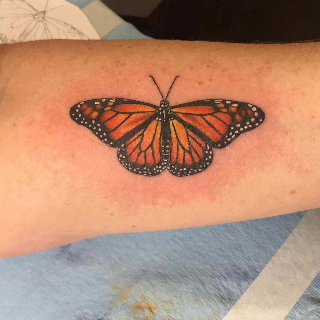 A realistic arm tattoo of a monarch butterfly, showcasing its vibrant orange and black wings
