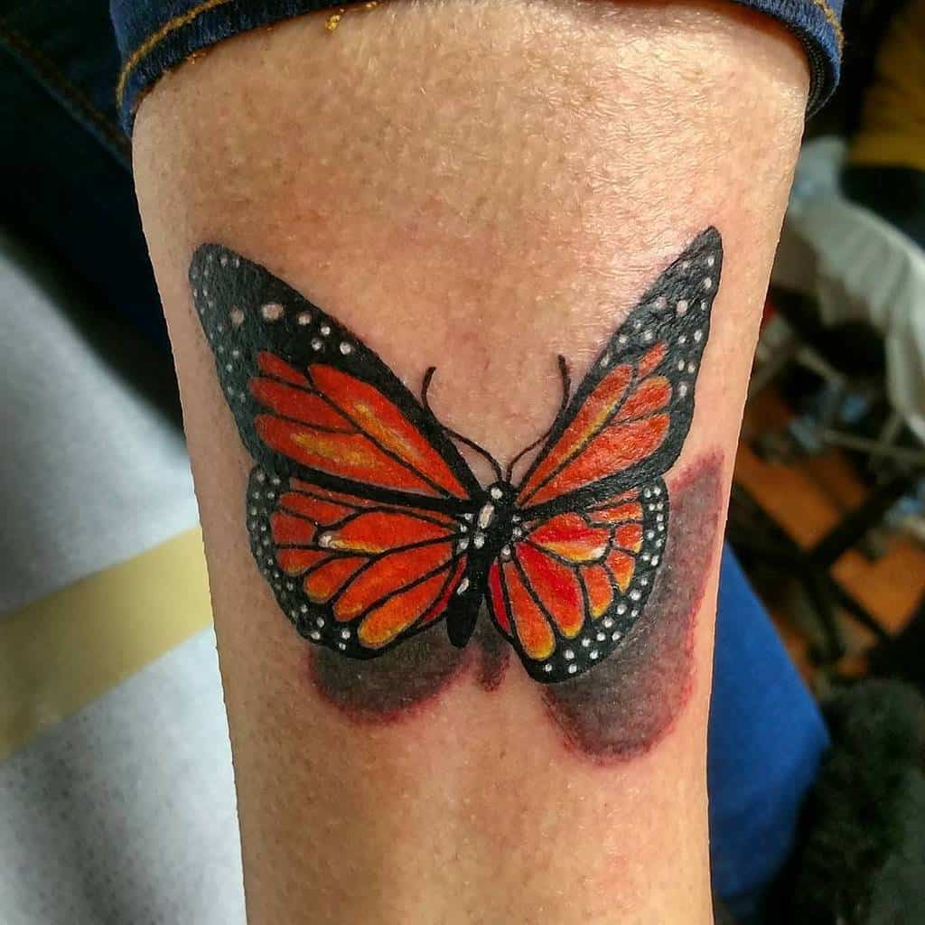 A vivid monarch butterfly tattoo in orange and black on the forearm, showcasing realistic details and shadow effects