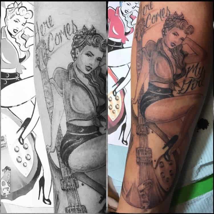 Black and white tattoo on forearm of a woman holding a guitar with text "Here Comes My Girl"