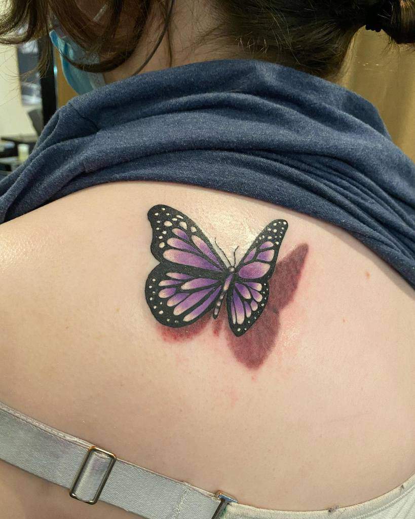 Woman's back with a purple and black butterfly tattoo close to her right shoulder
