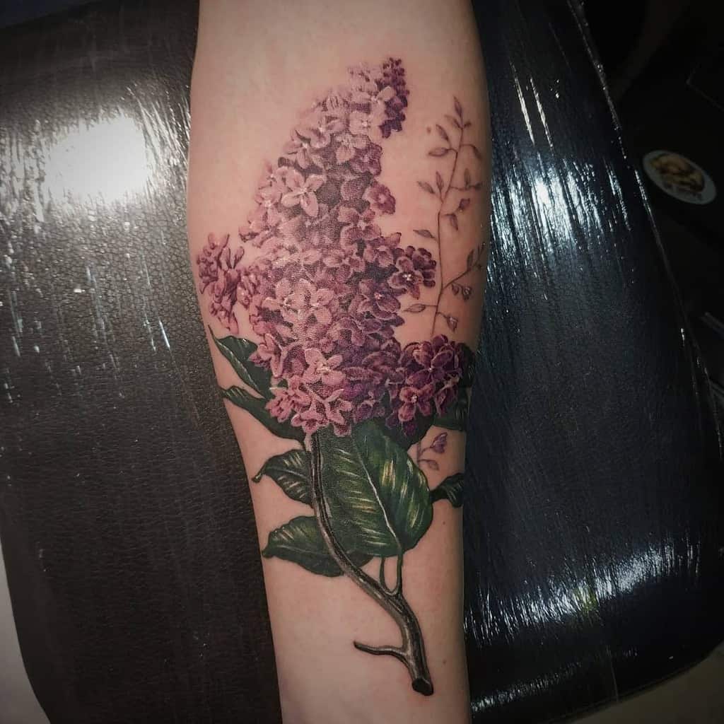 A tattoo of vibrant purple lilac flowers and lush green leaves on the forearm