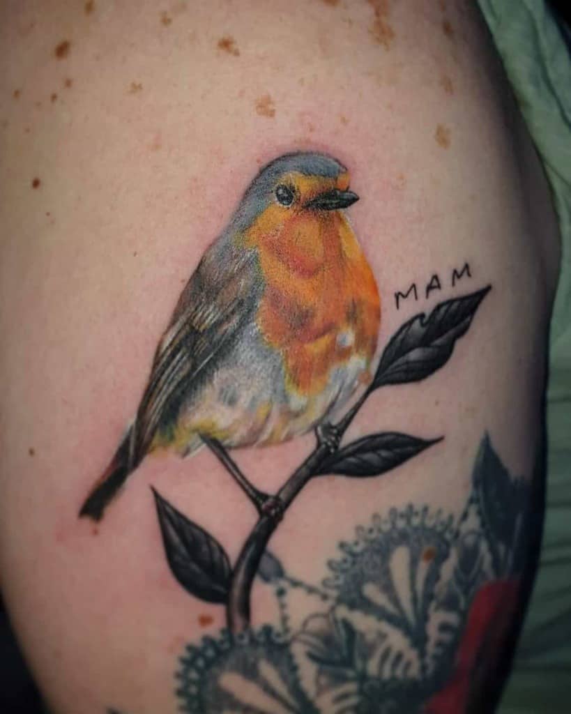 A tattoo of a colorful robin perched on a branch with "MAM" written next to it