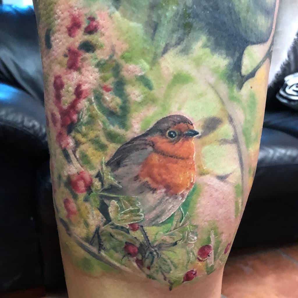 Tattoo of a robin perched on a branch with red berries, surrounded by a soft, blurred nature background