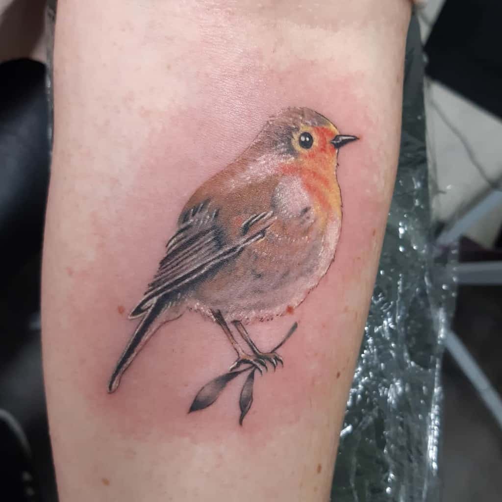 Realistic tattoo of a robin perched on a branch with leaves