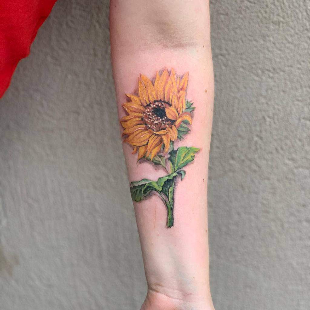 A colorful realistic sunflower tattoo on a forearm 