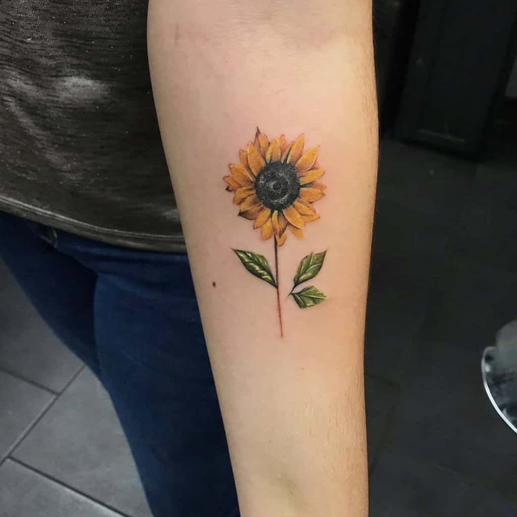 Forearm tattoo of a sunflower with two leaves, showing a realistic design and detailed colors