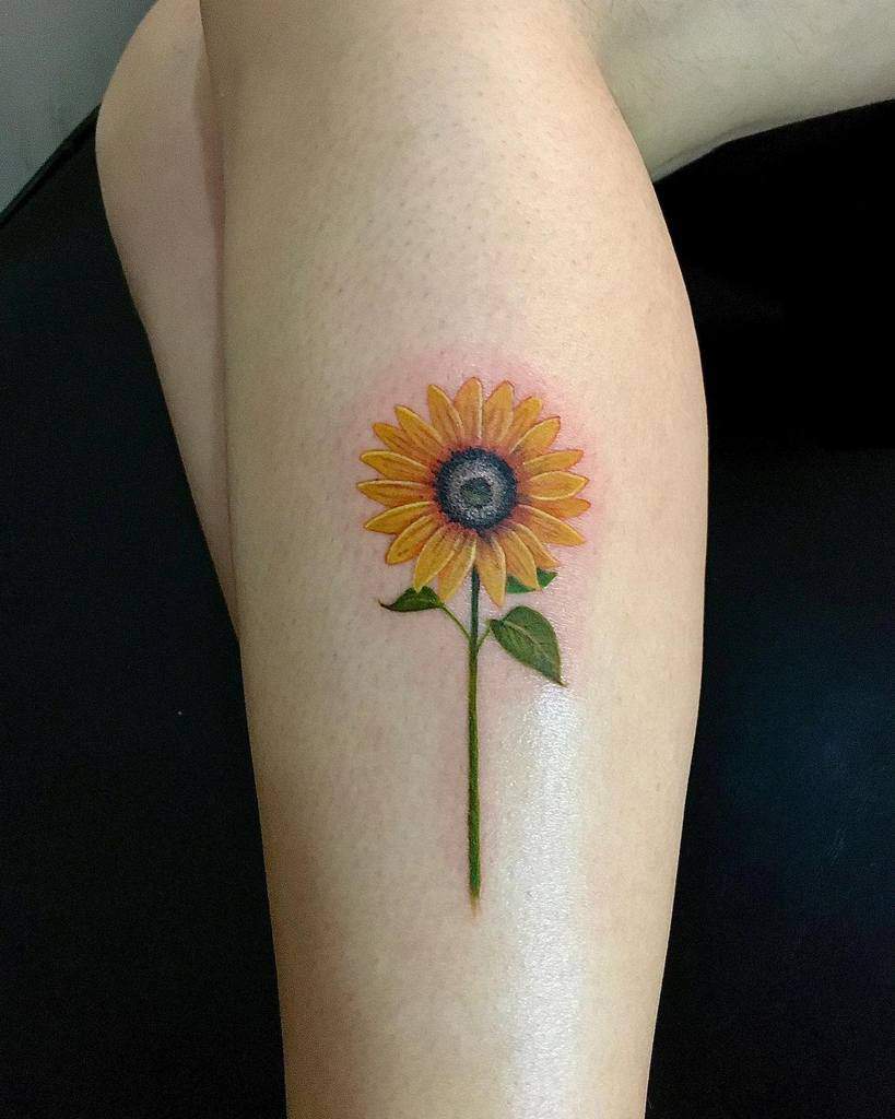 Tattoo of a sunflower with a stem and leaves on a calf