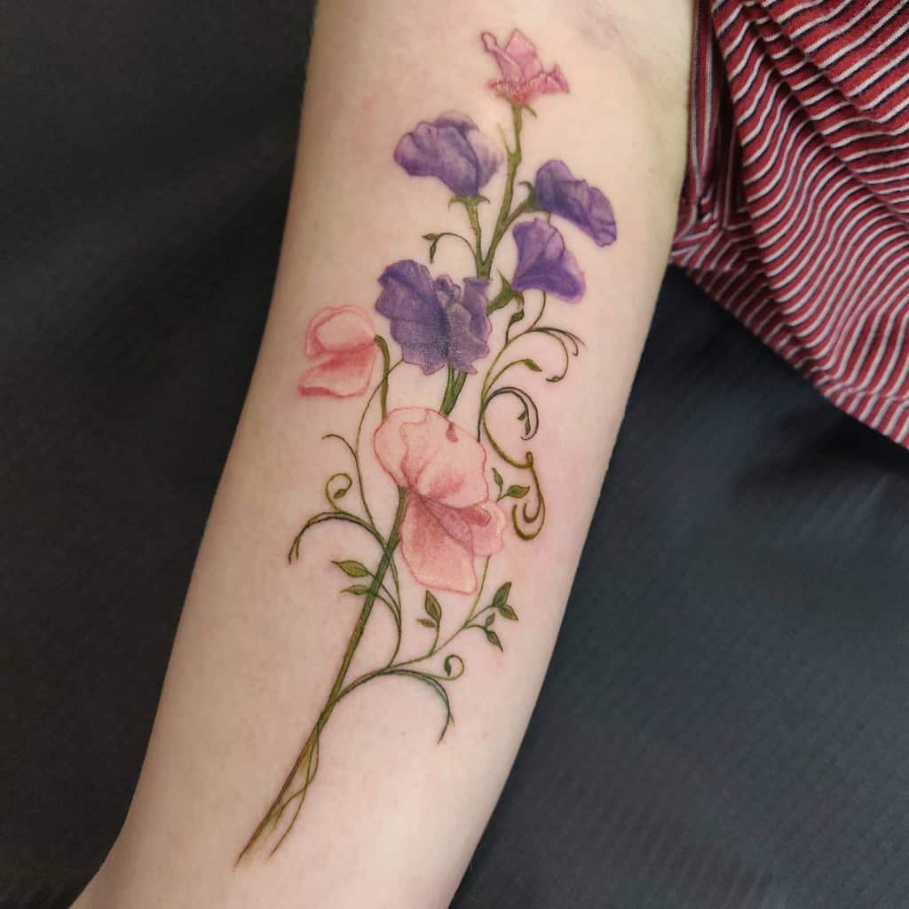 A realistic sweet pea tattoo with soft pink and purple blossoms, beautifully detailed on the forearm