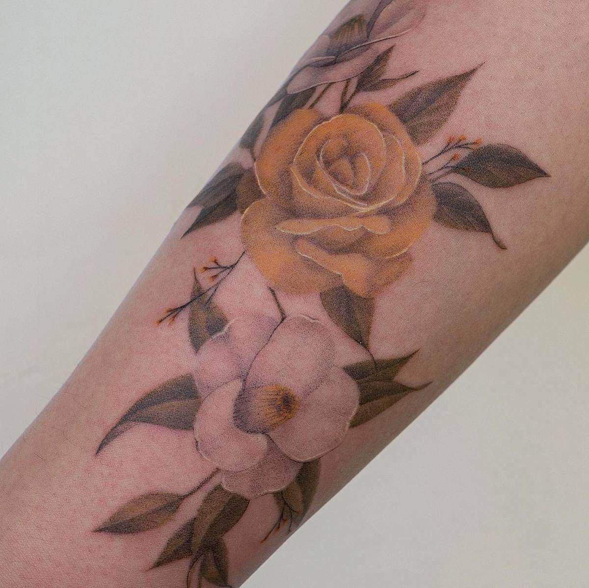 Forearm tattoo of detailed orange rose and white flower with green leaves
