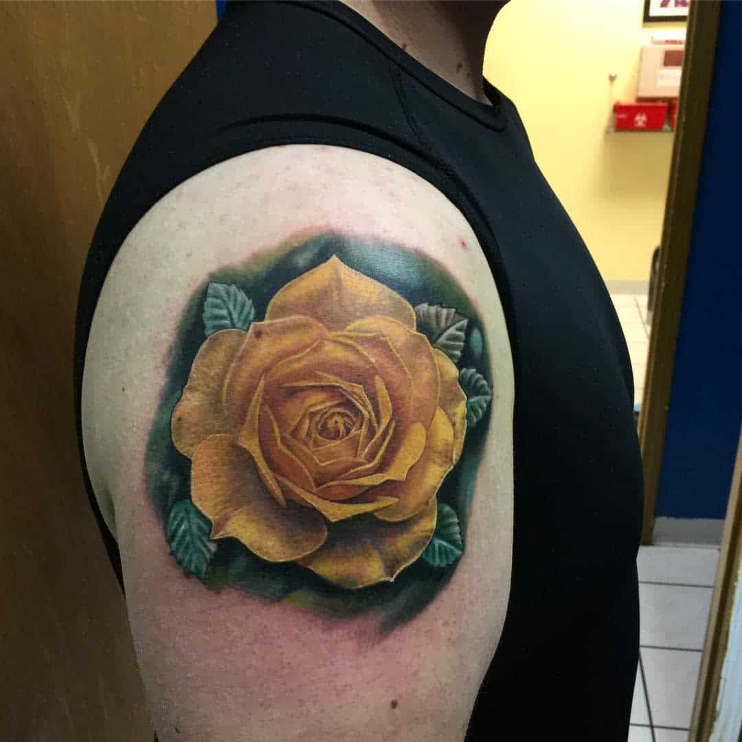 A yellow rose tattoo with green leaves is inked on the upper arm