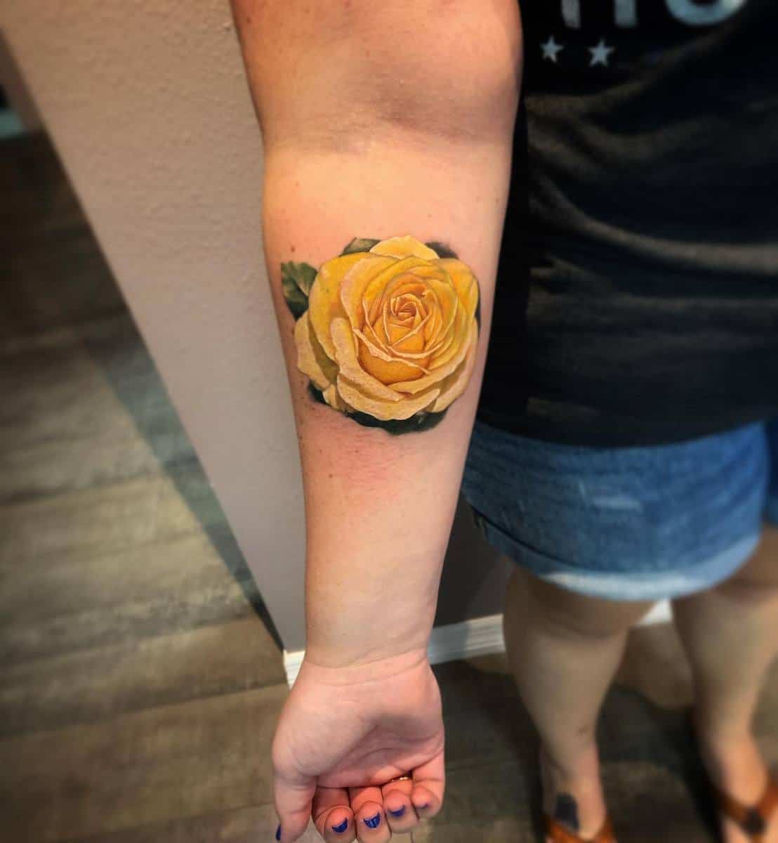Forearm tattoo of a yellow rose with green leaves