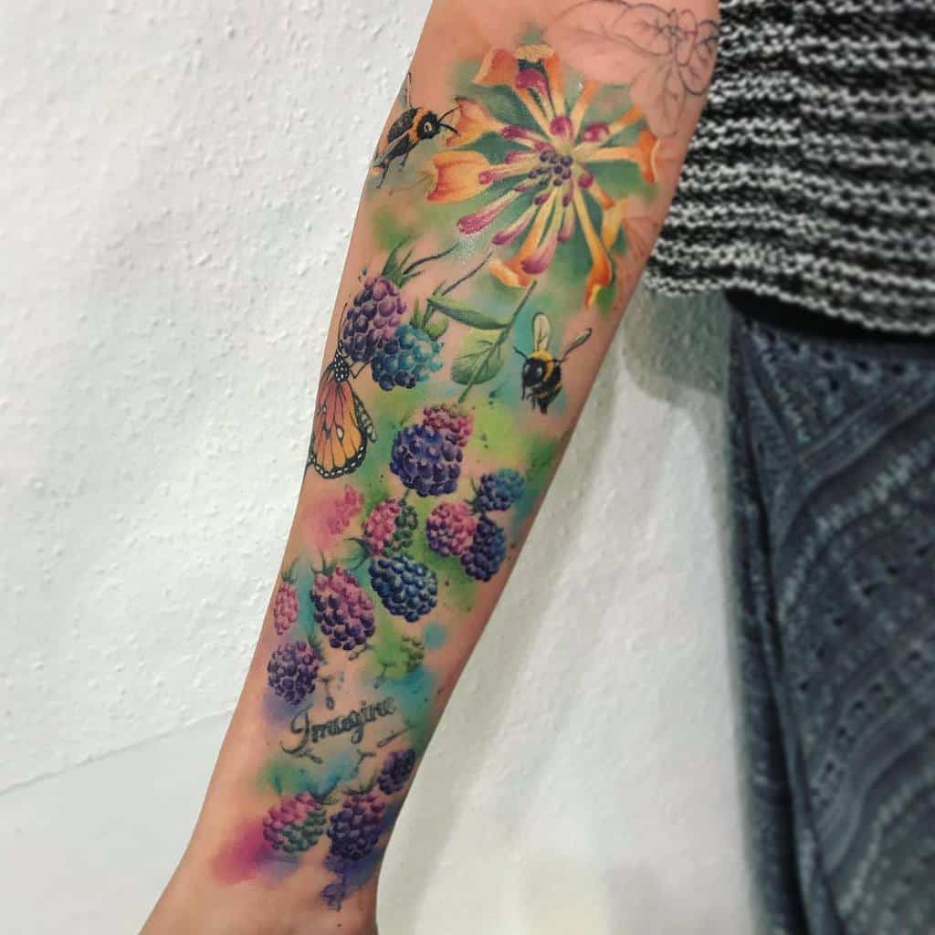 Forearm tattoo of flowers, honeysuckle, berries, bees, and a butterfly with the word 'Imagine' in script