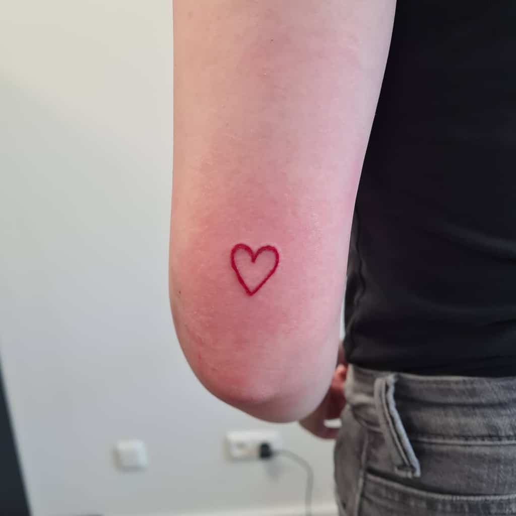 A small red heart outline tattoo on the back of a person's upper arm