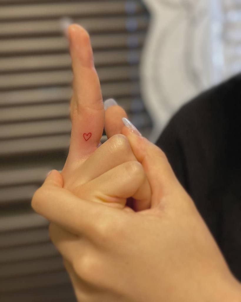A small heart outline tattoo on the side of a middle finger