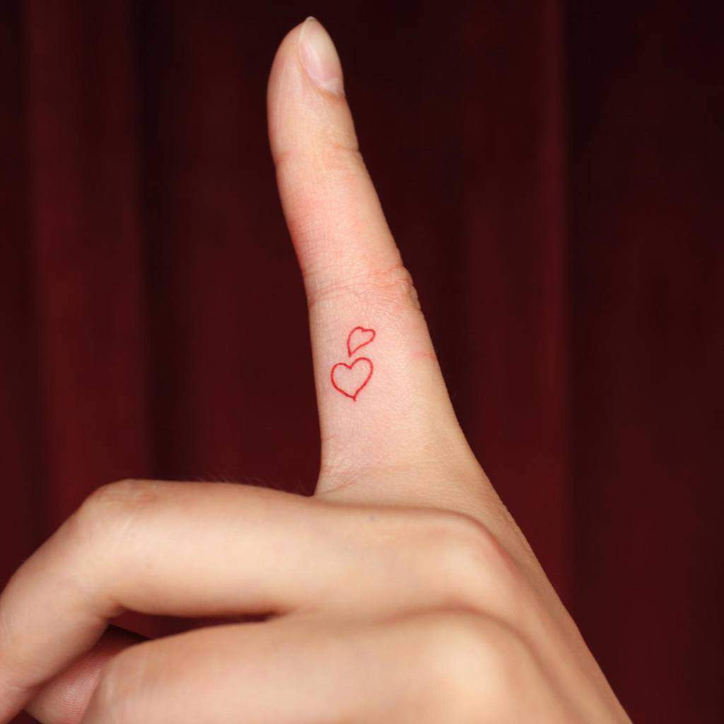 Hand with red heart outline tattoos on the side of the pinky finger