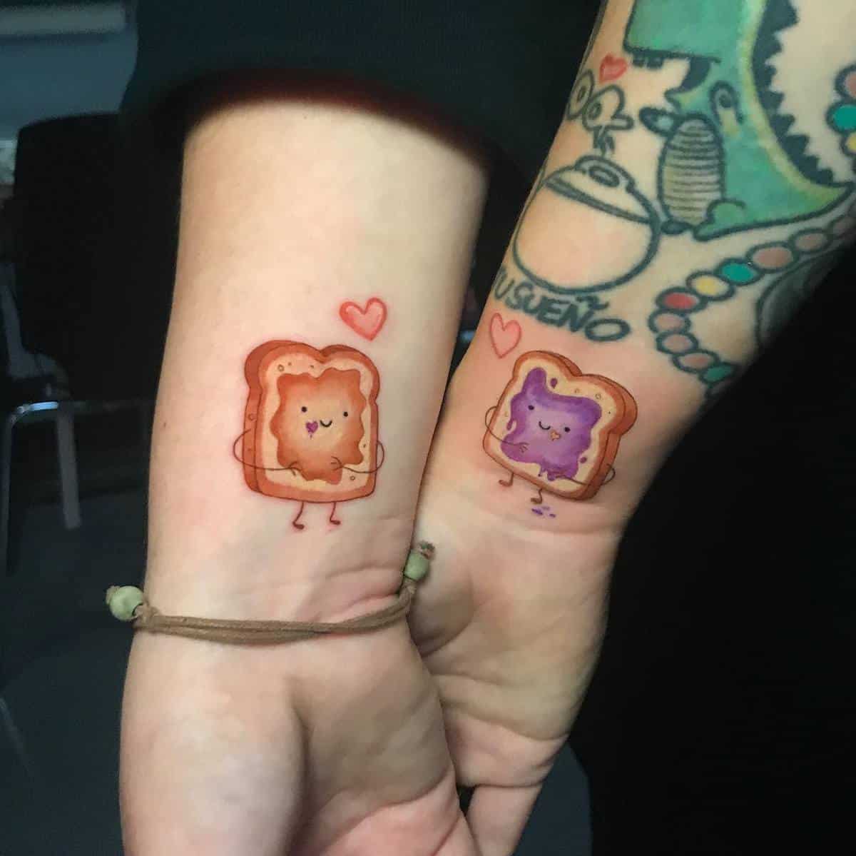 Two wrists with cute toast tattoos, one peanut butter and one jelly, each with a heart