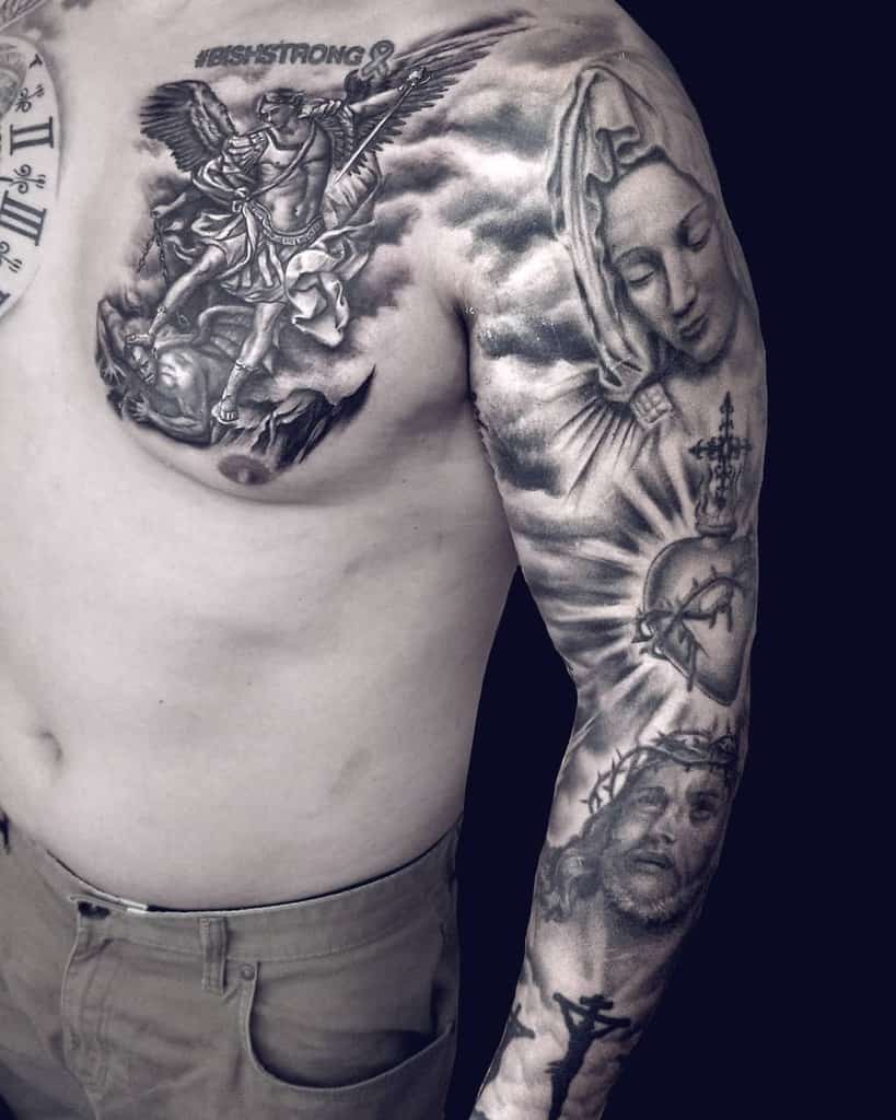 A religious-themed full sleeve tattoo in black and grey, featuring detailed portraits of Jesus, the Virgin Mary, sacred heart symbols, and clouds, with an angel defeating a demon on the chest