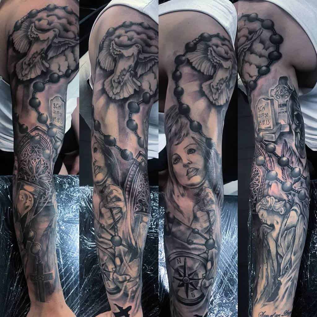 A black and grey full sleeve tattoo featuring religious themes, including a rosary, a dove, tombstones, and a detailed portrait of a woman, with intricate shading and symbolism throughout
