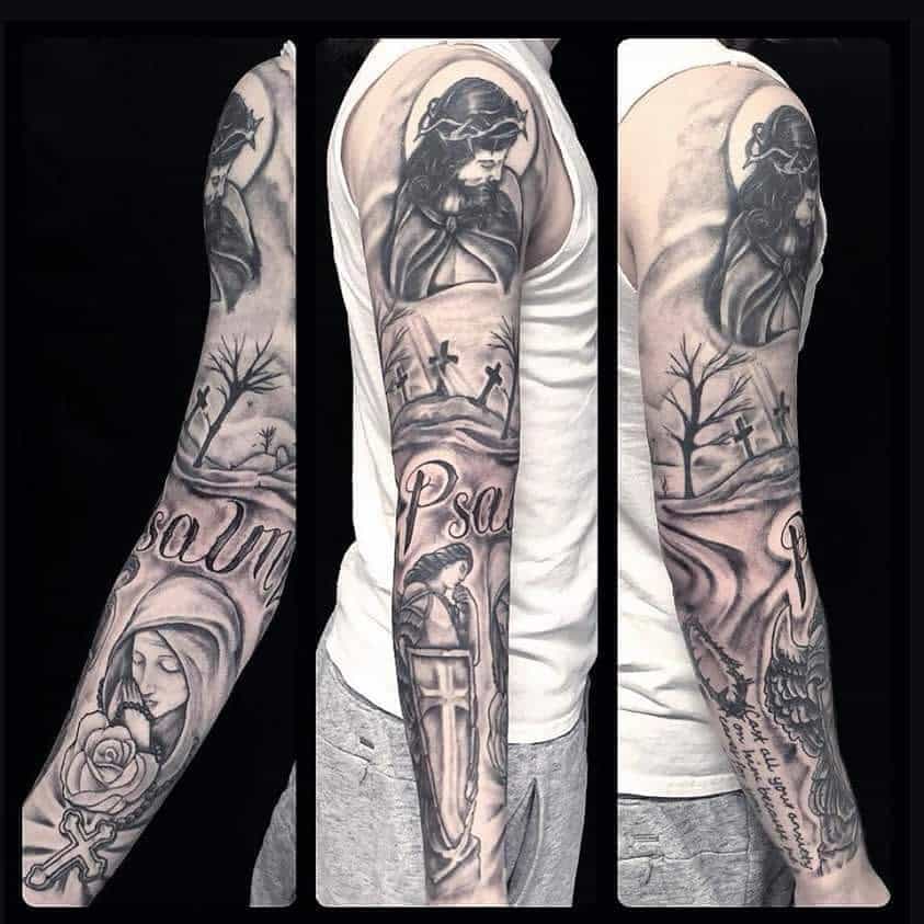 A black and grey full sleeve tattoo featuring religious imagery, including Jesus with a crown of thorns, a landscape with crosses, Psalm lettering, and a praying figure holding a rosary and rose
