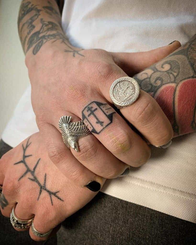 Hand tattoo featuring a bold cross on the middle finger and branch-like designs