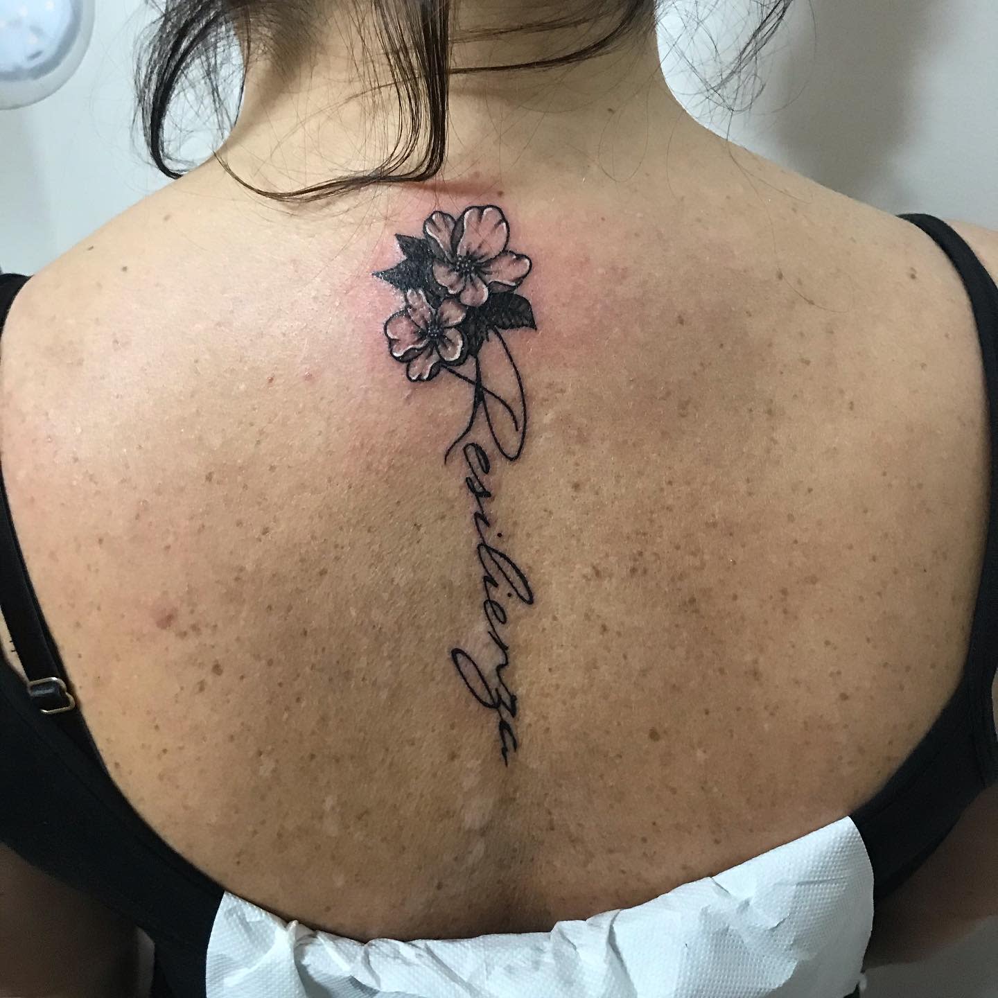 Tattoo of flowers and the word "Resilienza" on an upper back