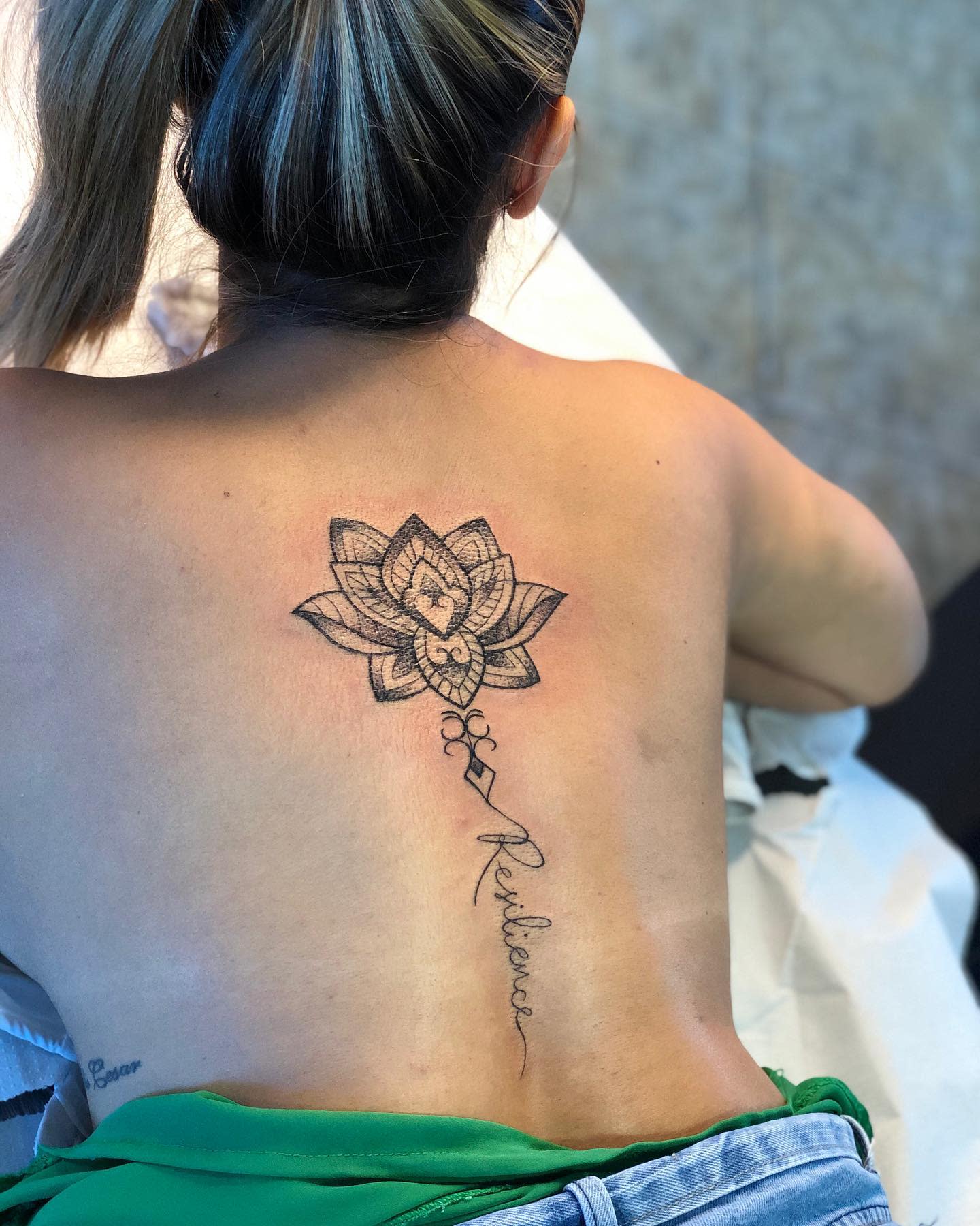 Woman with a detailed lotus tattoo and the word "Resilience" on her upper back