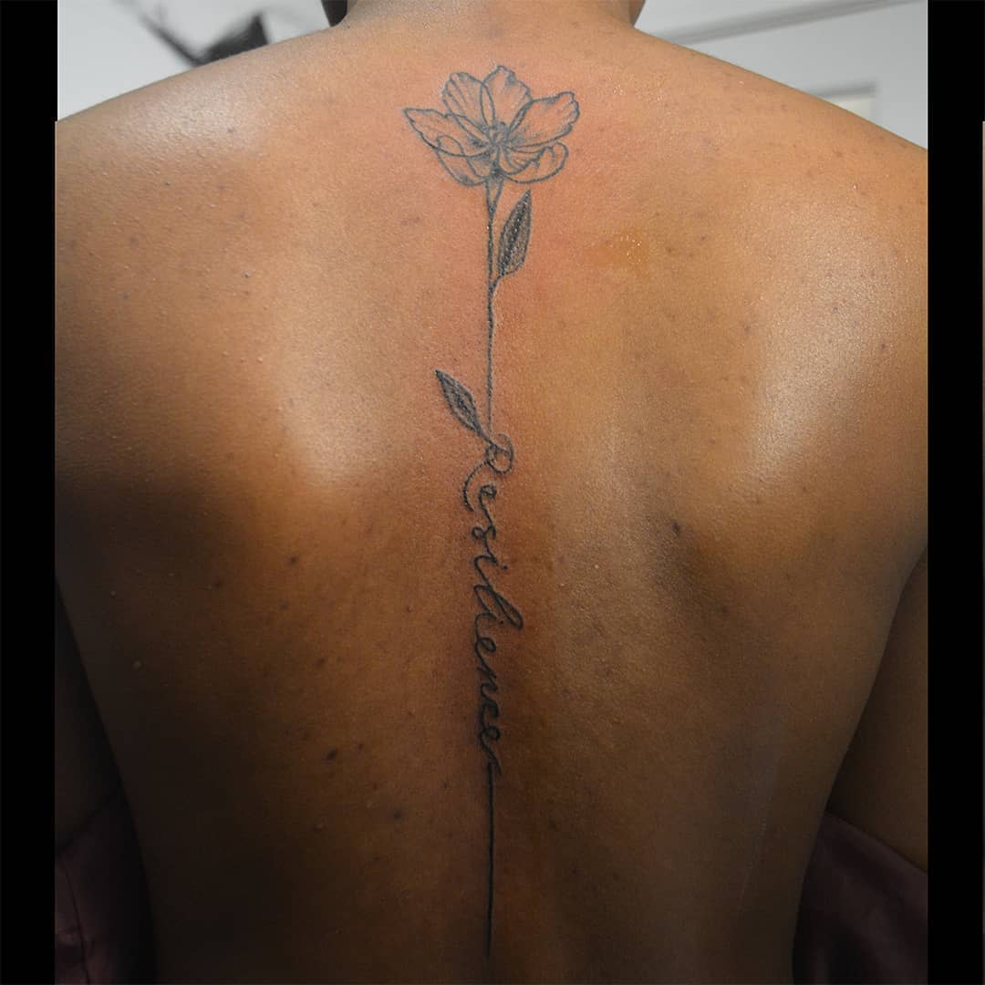 A tattoo of a flower and the word "Resilience" on back