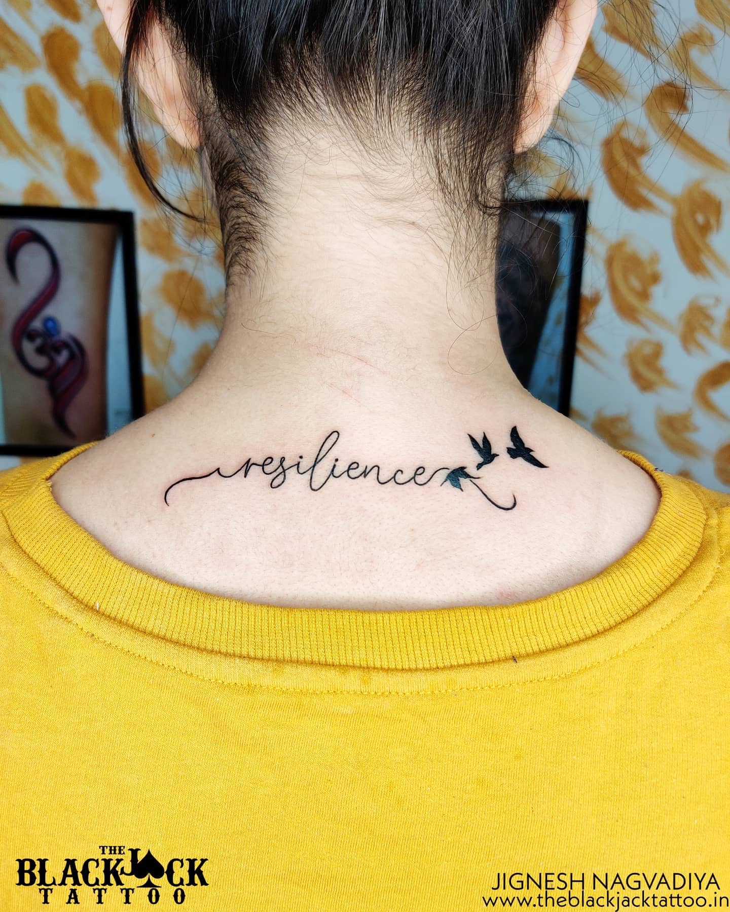Tattoo of "resilience" with flying birds on the back of the neck