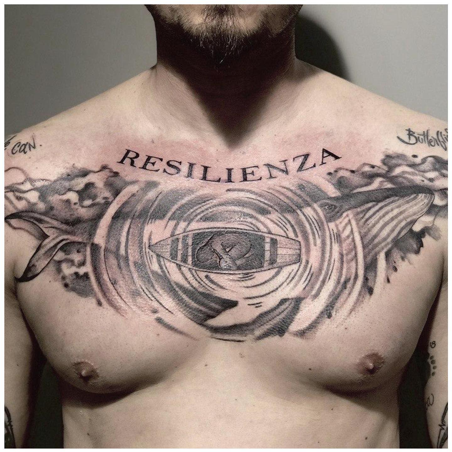 Man's chest tattoo featuring a a boat, waves, and a whale with "RESILIENZA" text above