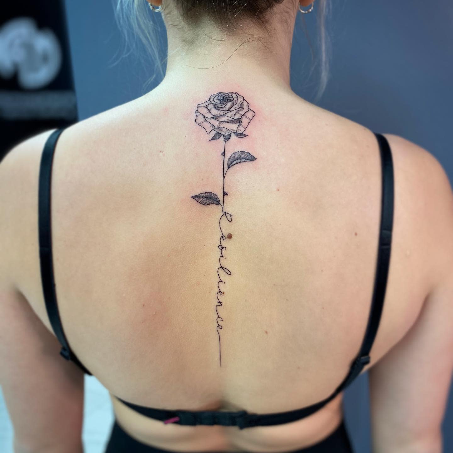 Rose tattoo extending spine with the word "resilience"