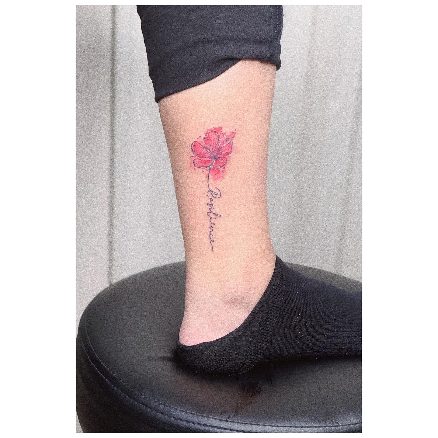 A leg with a red flower tattoo and cursive text "Resilience" on the ankle